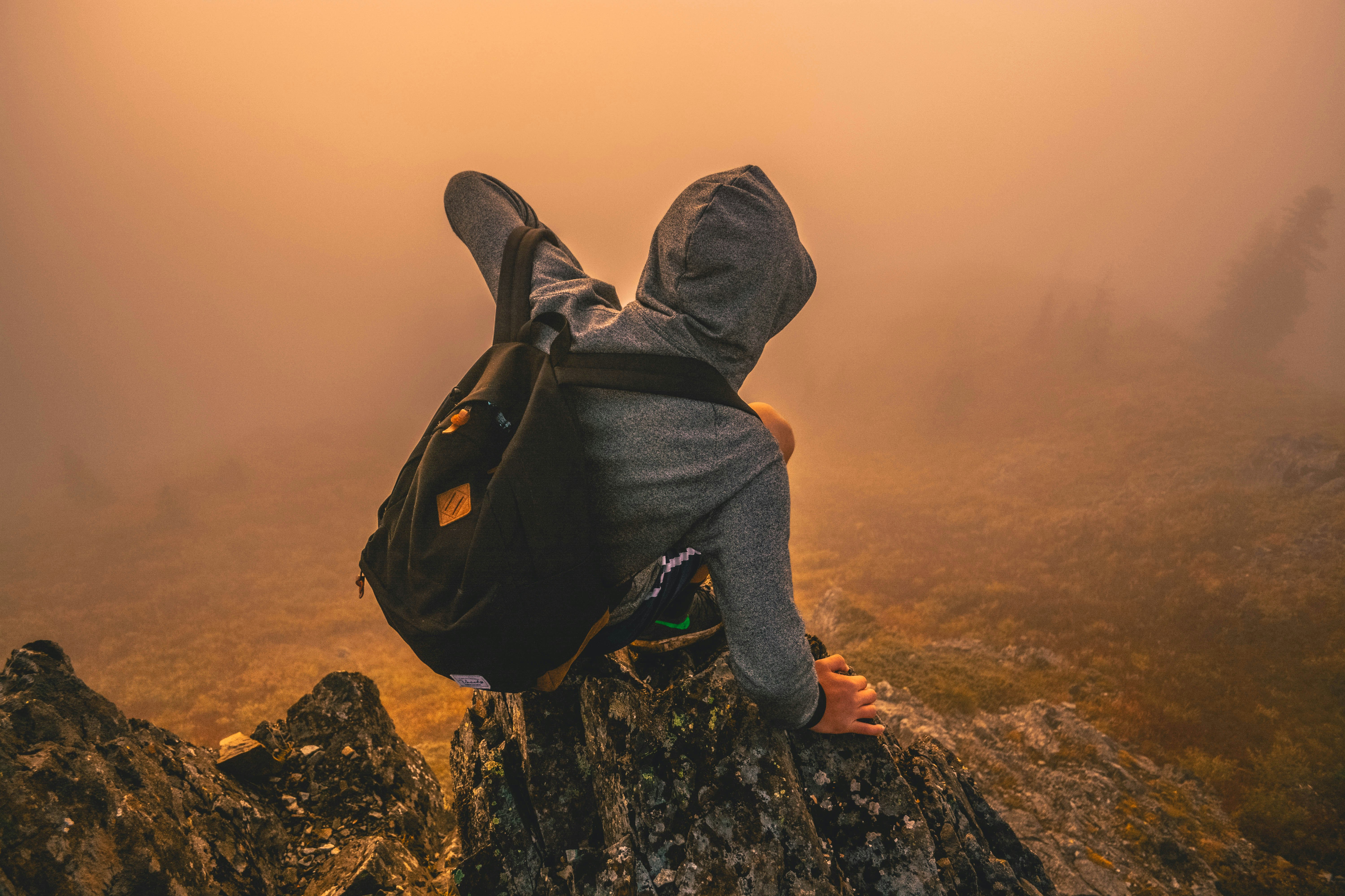 man in gray hoodie sitting on mountain during daytime